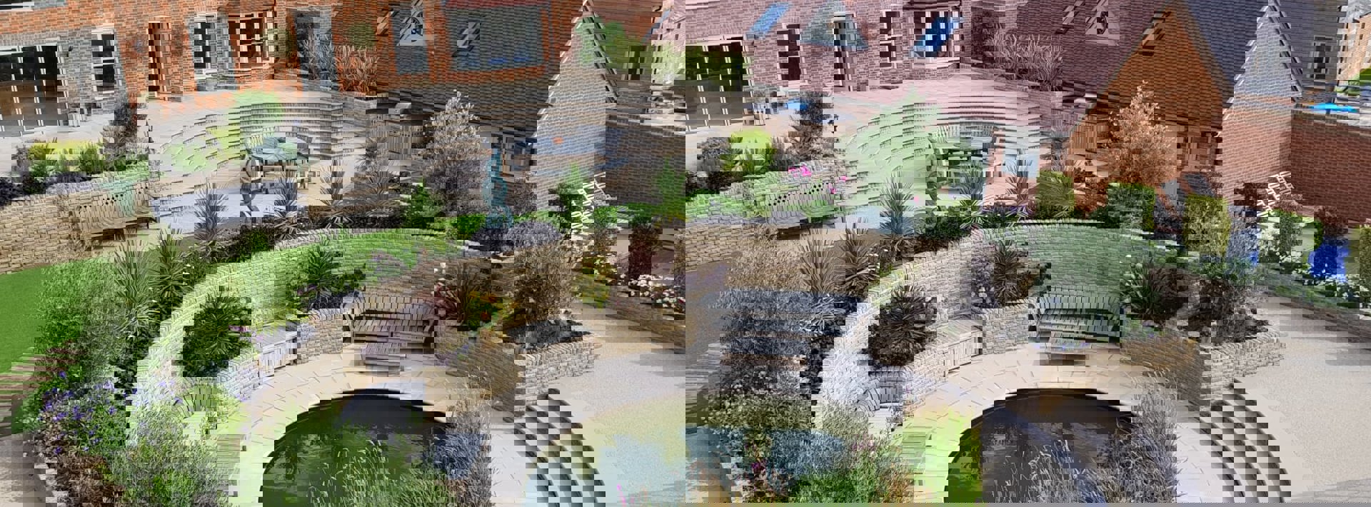 An aerial view of a garden with Marshalls Sawn Versuro paving and a circle feature with lots of greenery and wooden furniture