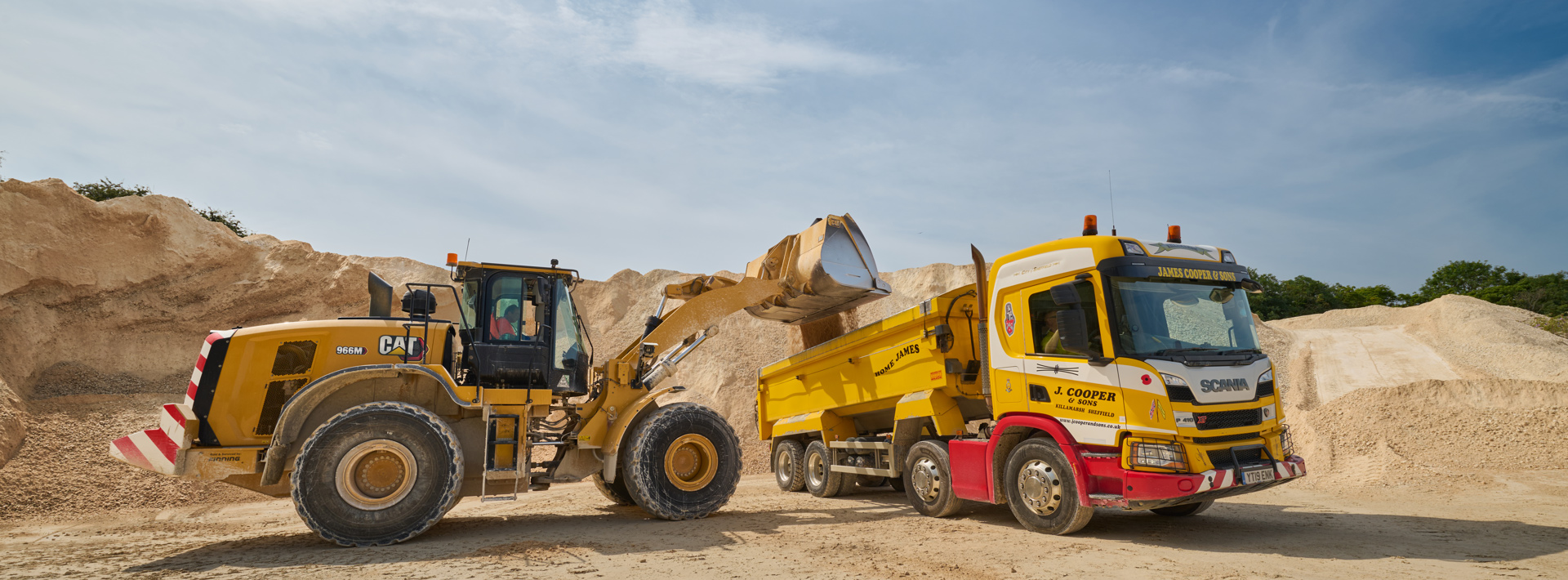 A digger off loading aggregates into a lorry on site